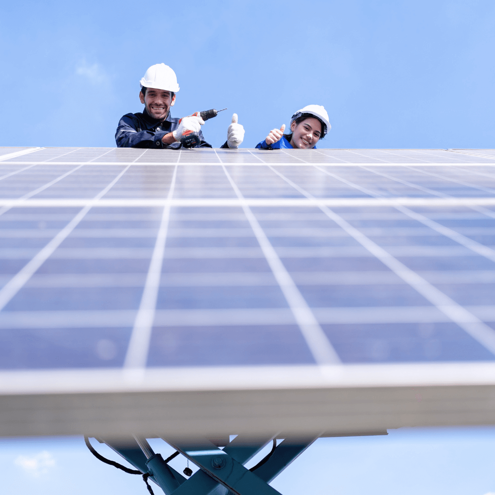Zwei Techniker mit weißen Helmen arbeiten an einer Photovoltaikanlage und zeigen Daumen hoch.